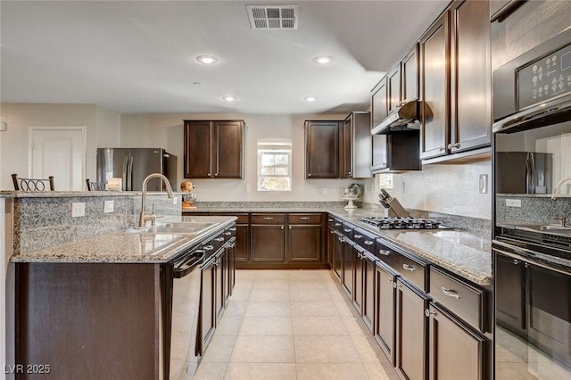 kitchen featuring light stone countertops, dark brown cabinetry, visible vents, a sink, and stainless steel appliances