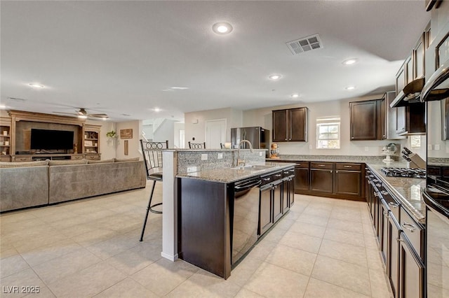kitchen with a kitchen breakfast bar, dark brown cabinets, black appliances, visible vents, and a sink