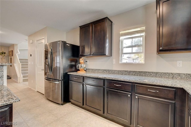 kitchen with light stone countertops, stainless steel refrigerator with ice dispenser, and dark brown cabinetry