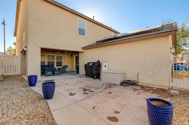 rear view of house featuring roof mounted solar panels, outdoor lounge area, fence, a patio, and stucco siding