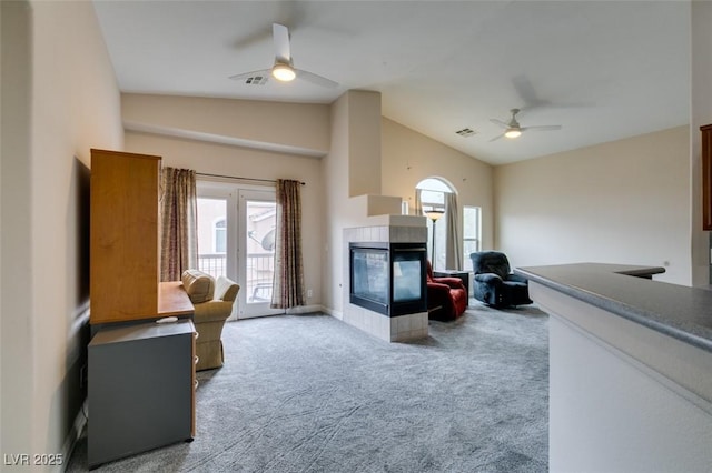 carpeted living area featuring high vaulted ceiling, a tile fireplace, visible vents, and a ceiling fan