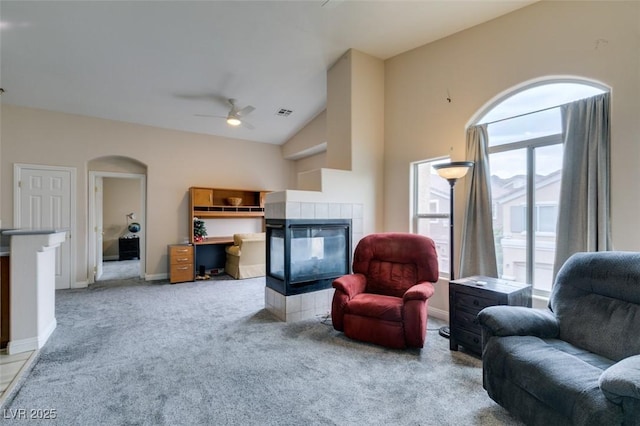 carpeted living area featuring arched walkways, a ceiling fan, a tiled fireplace, lofted ceiling, and baseboards