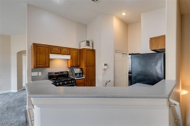 kitchen featuring freestanding refrigerator, arched walkways, light colored carpet, stainless steel gas range oven, and baseboards