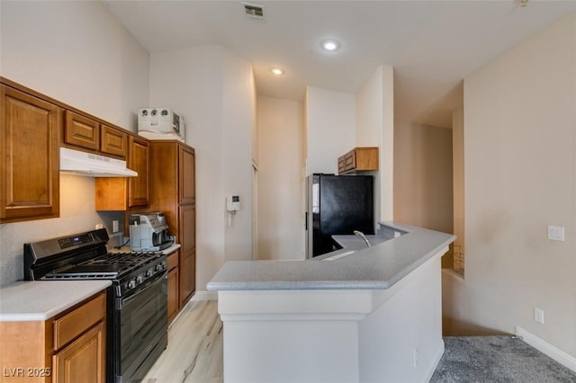 kitchen featuring a peninsula, under cabinet range hood, visible vents, brown cabinets, and black appliances
