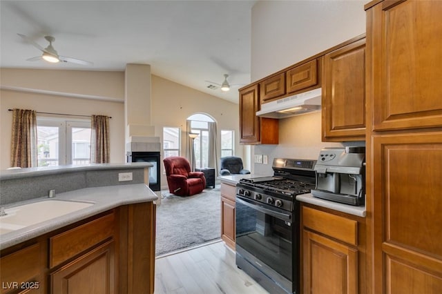kitchen featuring ceiling fan, a fireplace, under cabinet range hood, gas stove, and lofted ceiling