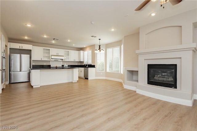 unfurnished living room featuring ceiling fan with notable chandelier, light wood-style flooring, visible vents, recessed lighting, and baseboards