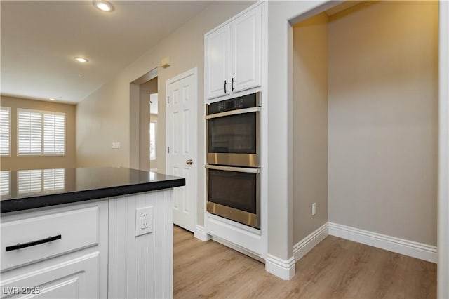 kitchen with dark countertops, white cabinets, double oven, and light wood finished floors