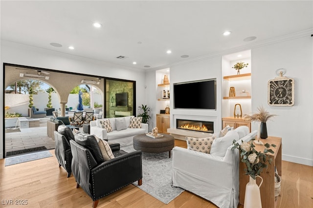 living room featuring crown molding, recessed lighting, light wood-style floors, a glass covered fireplace, and baseboards