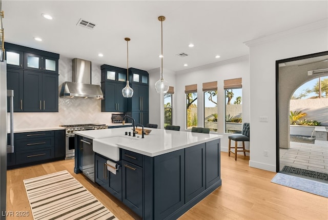 kitchen featuring wall chimney range hood, stainless steel stove, a sink, light countertops, and tasteful backsplash