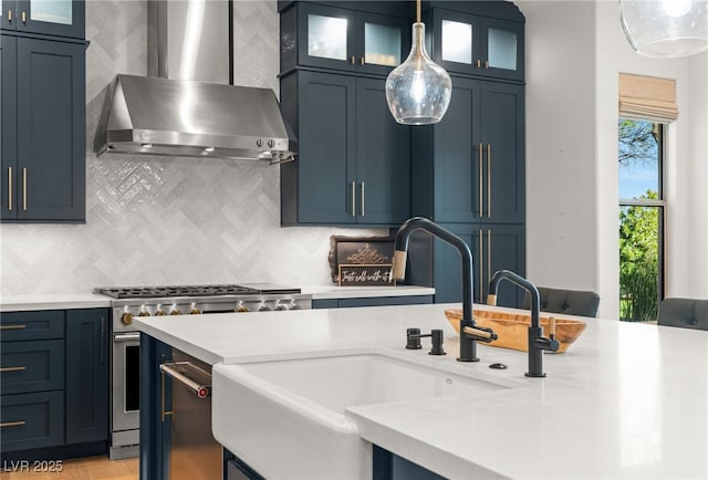 kitchen featuring wall chimney exhaust hood, high end stove, a sink, light countertops, and backsplash