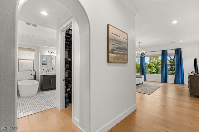 corridor featuring ornamental molding, arched walkways, light wood finished floors, a sink, and baseboards