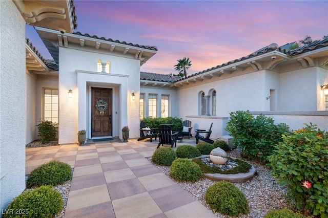 exterior entry at dusk with stucco siding and a tiled roof