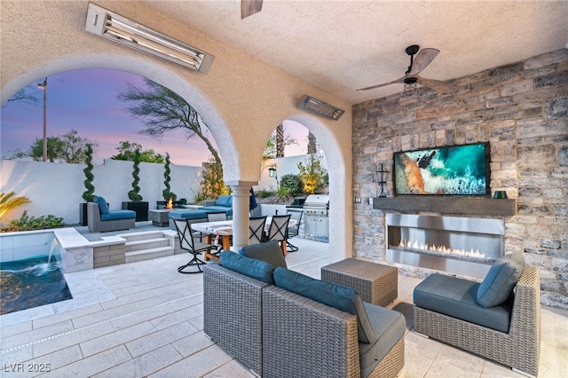 view of patio with an outdoor living space with a fireplace, ceiling fan, and exterior kitchen