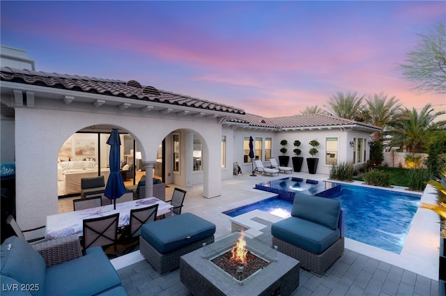 back of property featuring an outdoor living space with a fire pit, a patio, an outdoor pool, stucco siding, and an in-ground hot tub