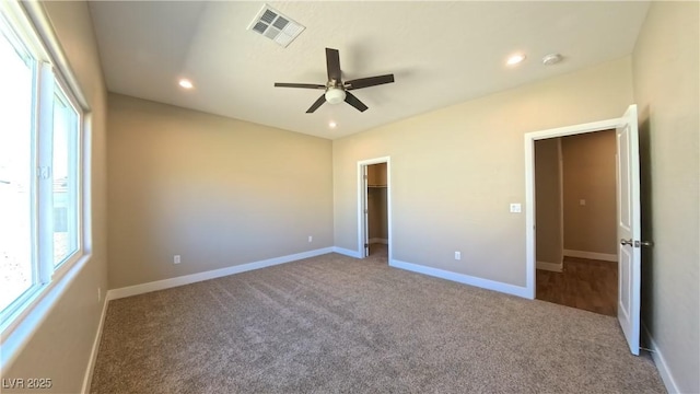 unfurnished bedroom featuring a walk in closet, carpet floors, recessed lighting, baseboards, and visible vents