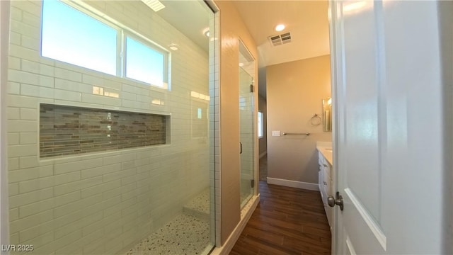 bathroom with vanity, baseboards, wood finished floors, visible vents, and a stall shower