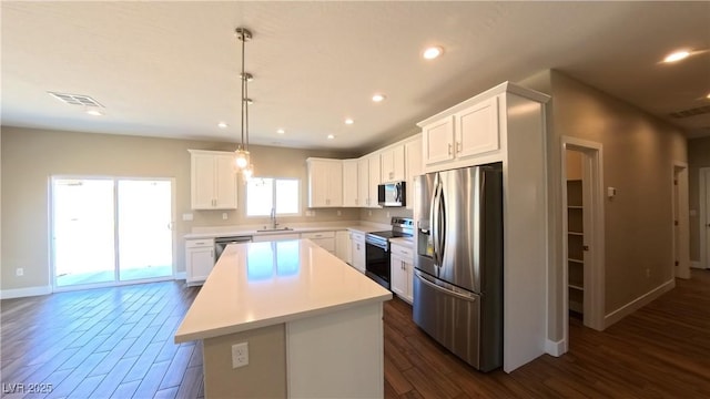 kitchen with appliances with stainless steel finishes, a sink, light countertops, dark wood finished floors, and a kitchen island
