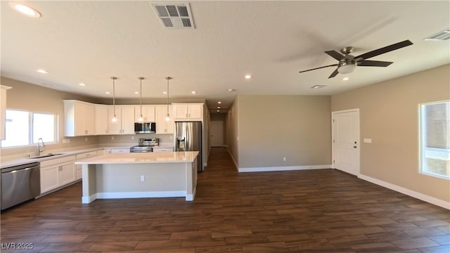 kitchen featuring visible vents, a ceiling fan, a kitchen island, a sink, and appliances with stainless steel finishes