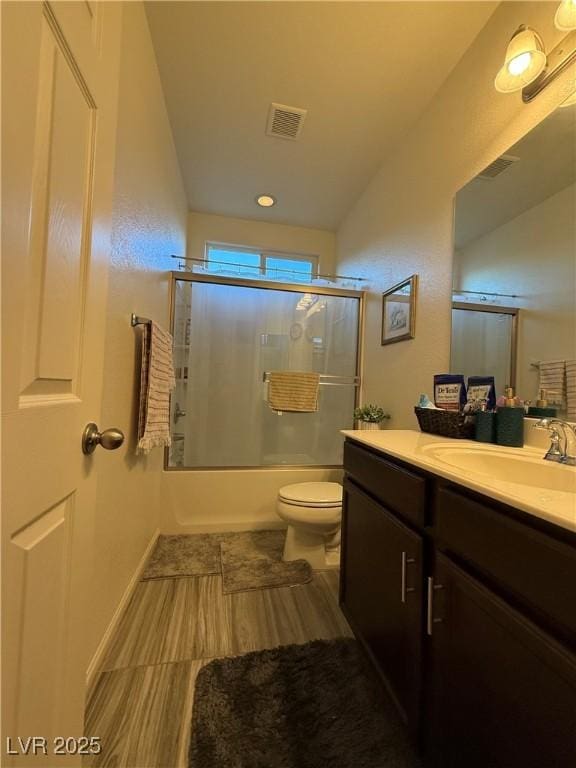 bathroom featuring combined bath / shower with glass door, vanity, visible vents, and toilet