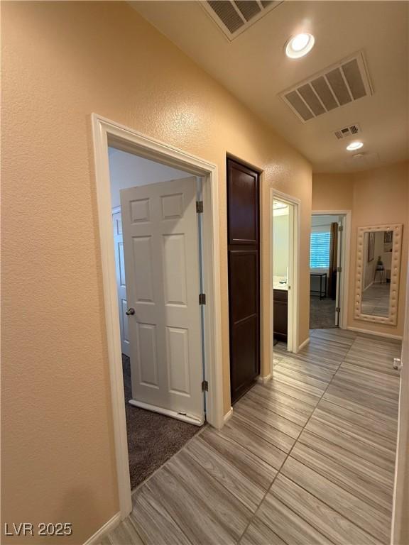hall featuring visible vents, recessed lighting, and a textured wall