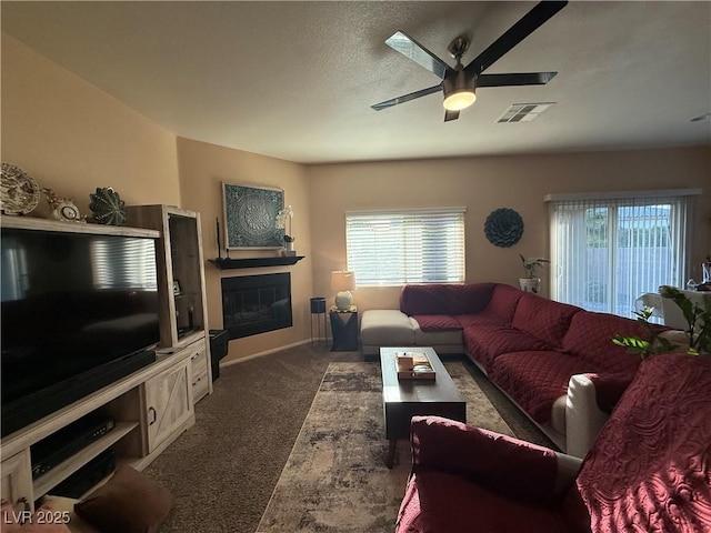 living room featuring a glass covered fireplace, a wealth of natural light, a ceiling fan, and carpet floors
