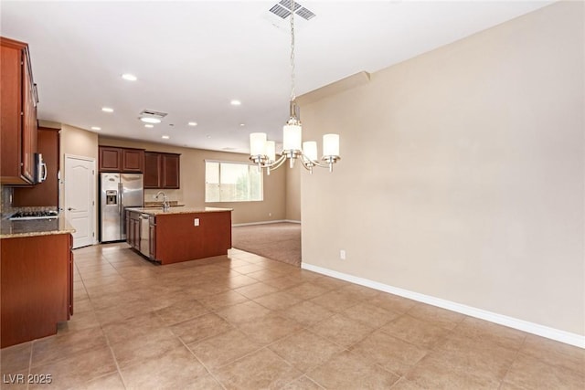 kitchen featuring a chandelier, a kitchen island with sink, a sink, stainless steel appliances, and baseboards