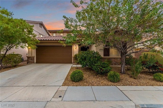 mediterranean / spanish-style house with an attached garage, stucco siding, stone siding, and concrete driveway