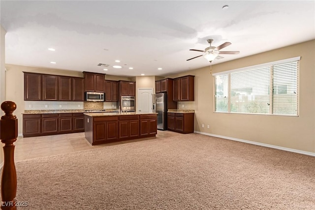 kitchen with baseboards, open floor plan, appliances with stainless steel finishes, dark brown cabinetry, and decorative backsplash