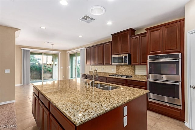 kitchen with an island with sink, visible vents, appliances with stainless steel finishes, a sink, and decorative backsplash