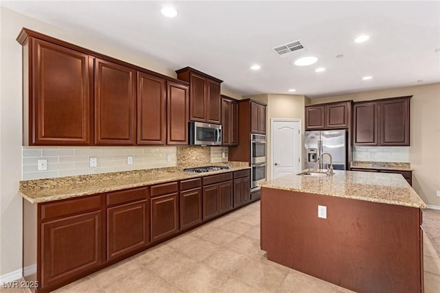 kitchen with tasteful backsplash, an island with sink, visible vents, appliances with stainless steel finishes, and a sink