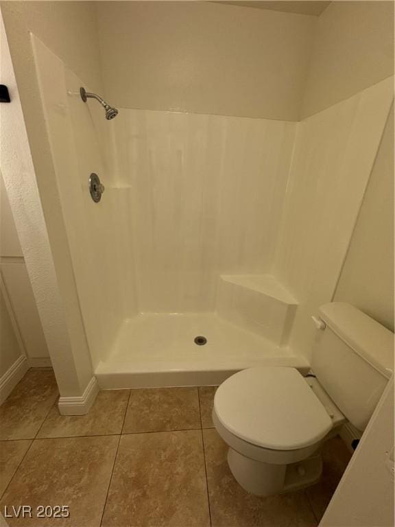 bathroom with toilet, baseboards, tile patterned flooring, and a stall shower