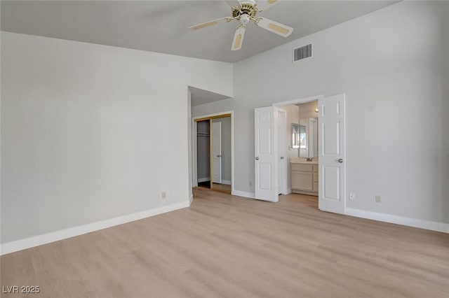 unfurnished bedroom featuring visible vents, baseboards, ensuite bathroom, light wood-type flooring, and vaulted ceiling