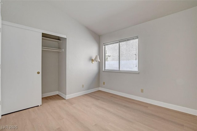 unfurnished bedroom with light wood-style floors, a closet, baseboards, and vaulted ceiling