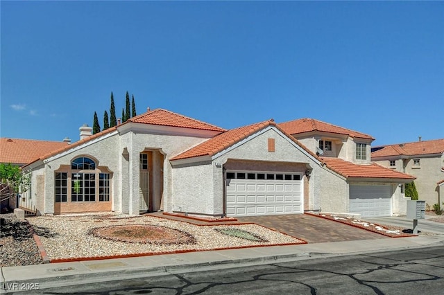 mediterranean / spanish house featuring an attached garage, aphalt driveway, stucco siding, and a tile roof
