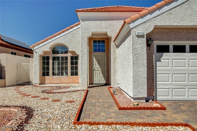 entrance to property with a tile roof, a garage, and stucco siding