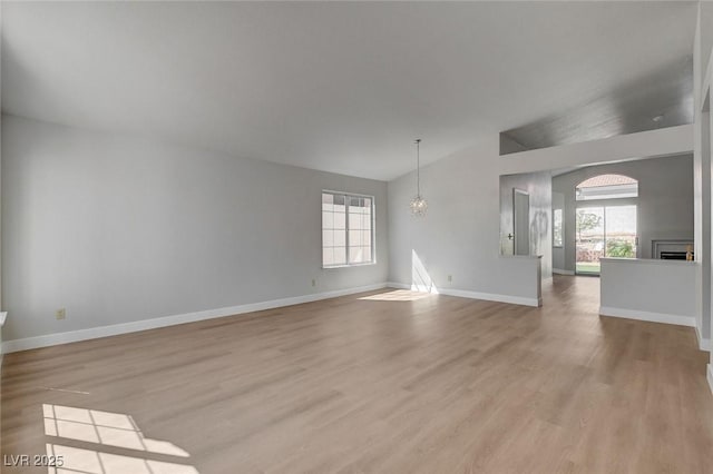 unfurnished living room featuring plenty of natural light, baseboards, wood finished floors, and lofted ceiling