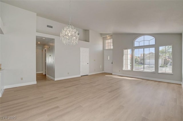 unfurnished living room with baseboards, an inviting chandelier, light wood-style flooring, a high ceiling, and visible vents