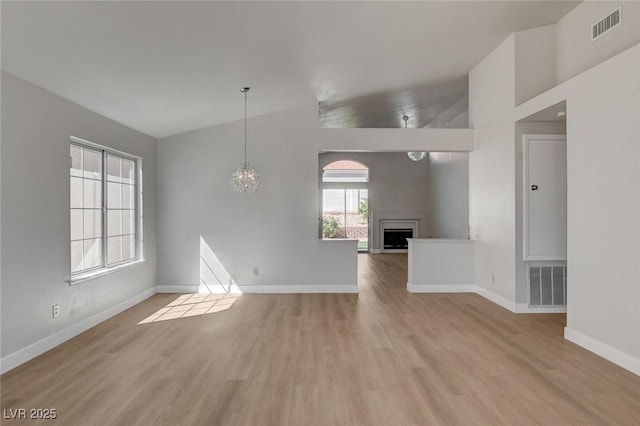 unfurnished living room with a notable chandelier, baseboards, a fireplace, visible vents, and light wood finished floors