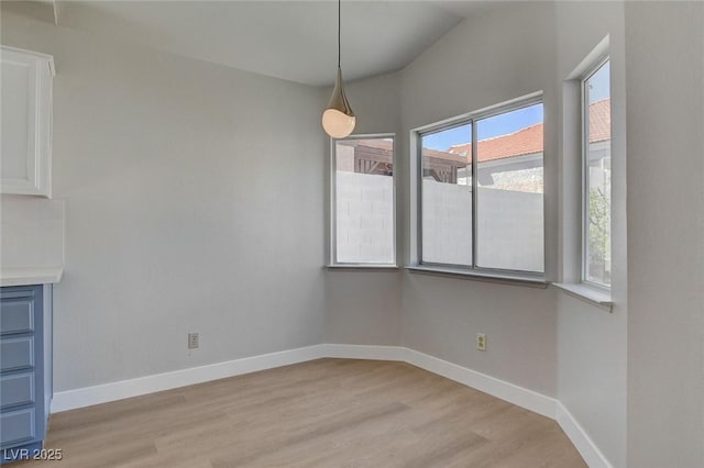 unfurnished dining area featuring baseboards, light wood-type flooring, and vaulted ceiling