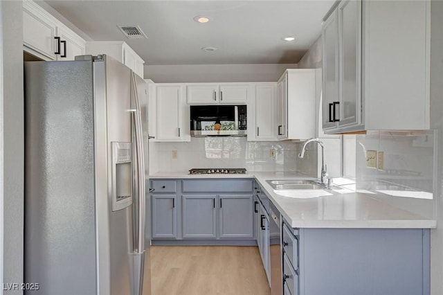 kitchen with gray cabinets, light wood-style floors, appliances with stainless steel finishes, and a sink