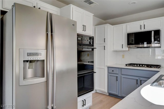 kitchen with visible vents, white cabinets, light wood-style floors, stainless steel appliances, and decorative backsplash