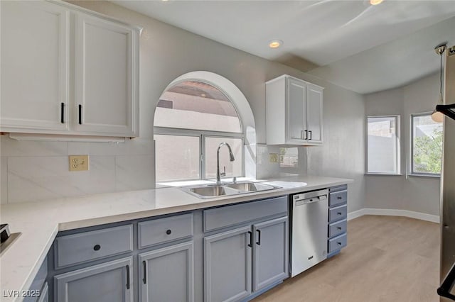 kitchen featuring light wood-style floors, stainless steel dishwasher, a sink, decorative backsplash, and gray cabinetry