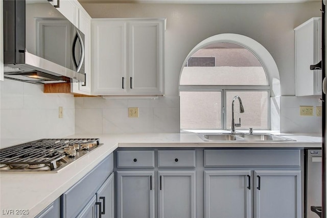 kitchen with tasteful backsplash, light countertops, a sink, stainless steel appliances, and gray cabinetry