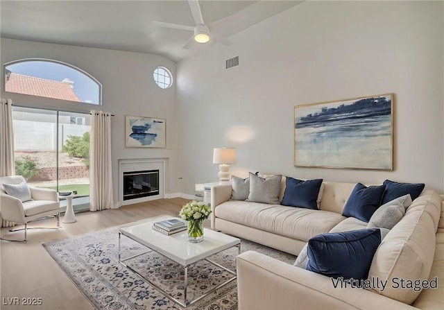 living room featuring visible vents, a ceiling fan, wood finished floors, high vaulted ceiling, and a glass covered fireplace