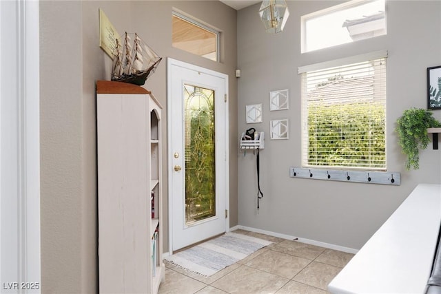 entryway with baseboards, light tile patterned flooring, and a towering ceiling