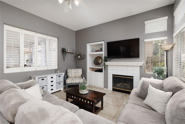 living room featuring built in features, light tile patterned floors, a tiled fireplace, and a ceiling fan