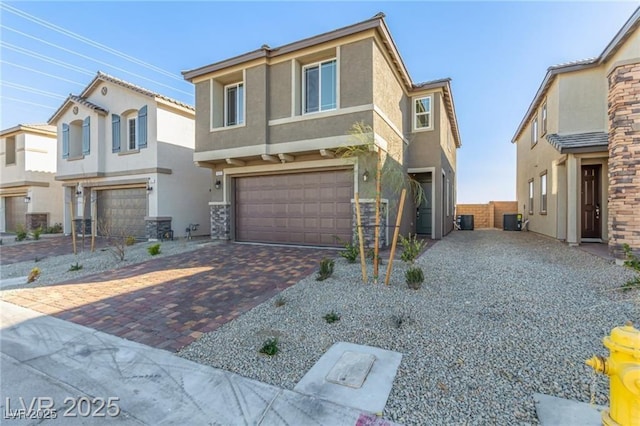 view of front of house with an attached garage, stucco siding, central AC unit, and decorative driveway