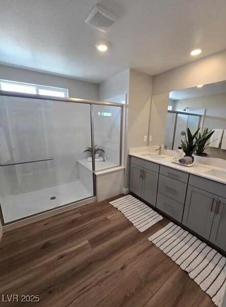 full bath with visible vents, double vanity, a stall shower, and wood finished floors