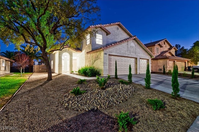 mediterranean / spanish-style home featuring stucco siding, driveway, a tile roof, a garage, and fence