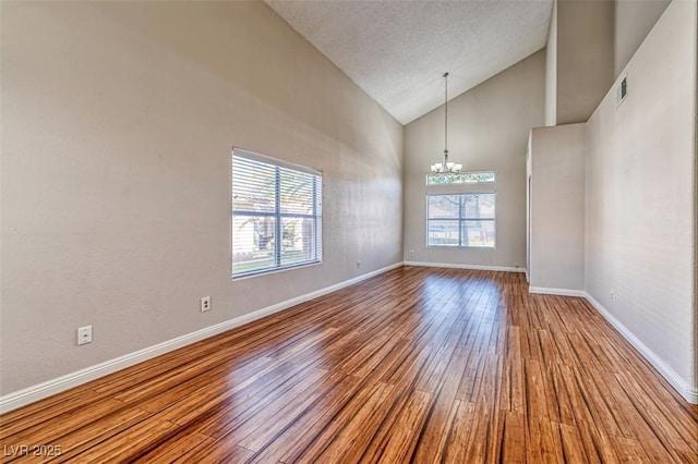 spare room featuring baseboards, an inviting chandelier, visible vents, high vaulted ceiling, and wood finished floors